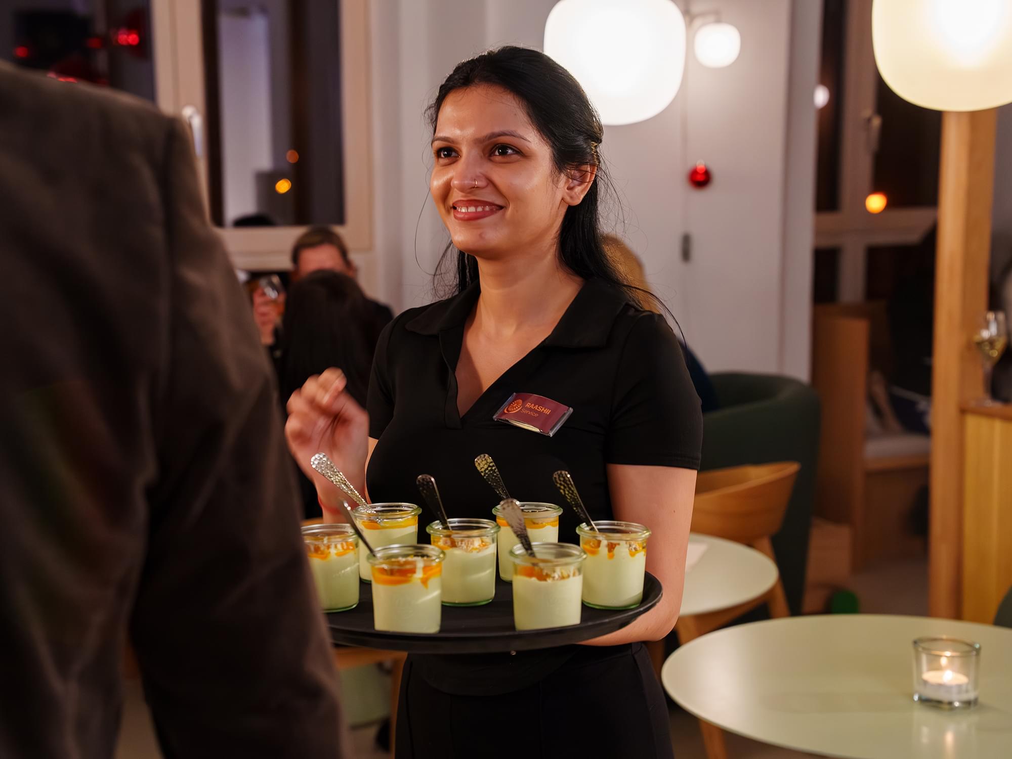 Servicekraft serviert Desserts im Glas beim Catering von AMRIT