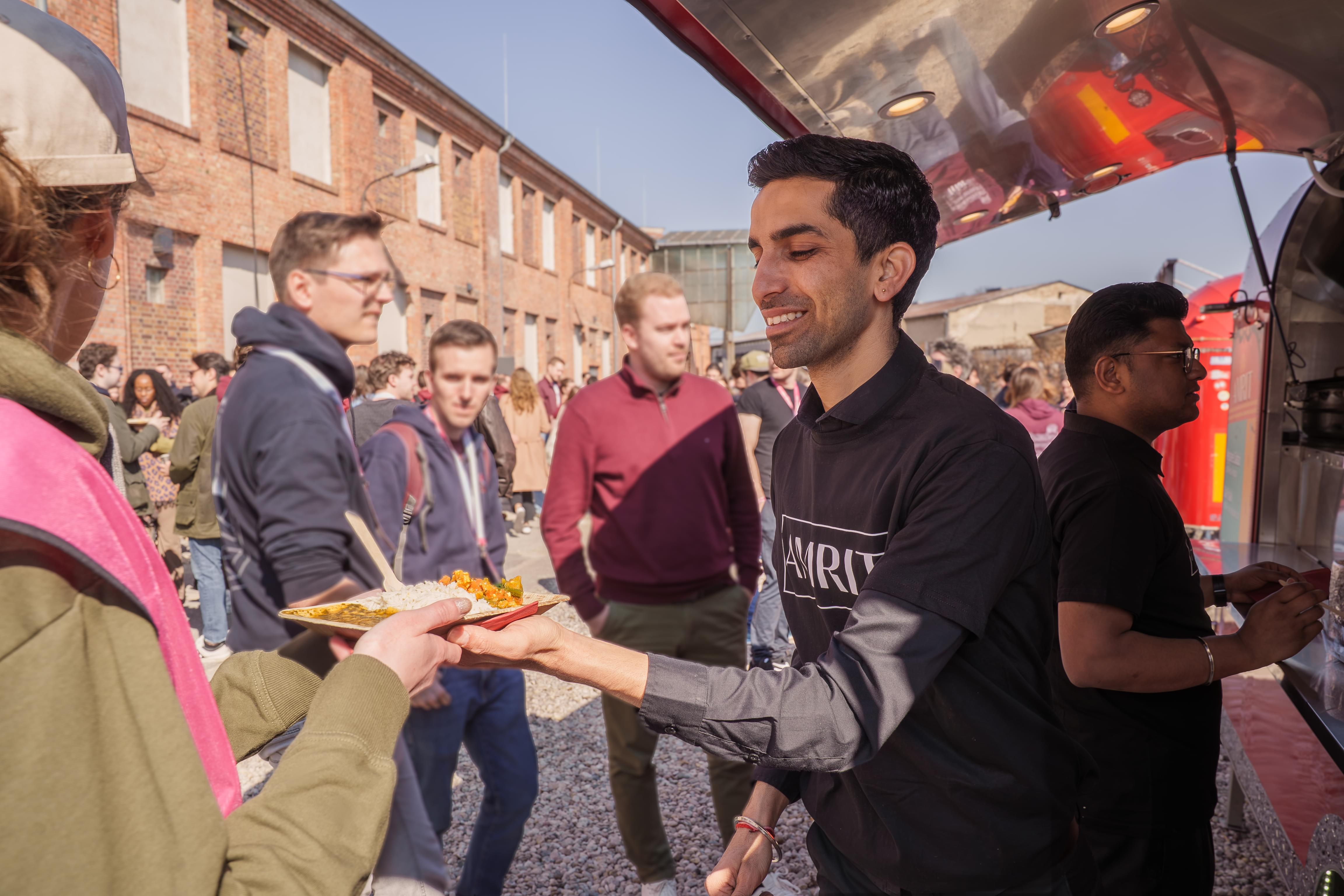 AMRIT Mitarbeiter reicht indisches Streetfood aus dem Foodtruck an Gäste