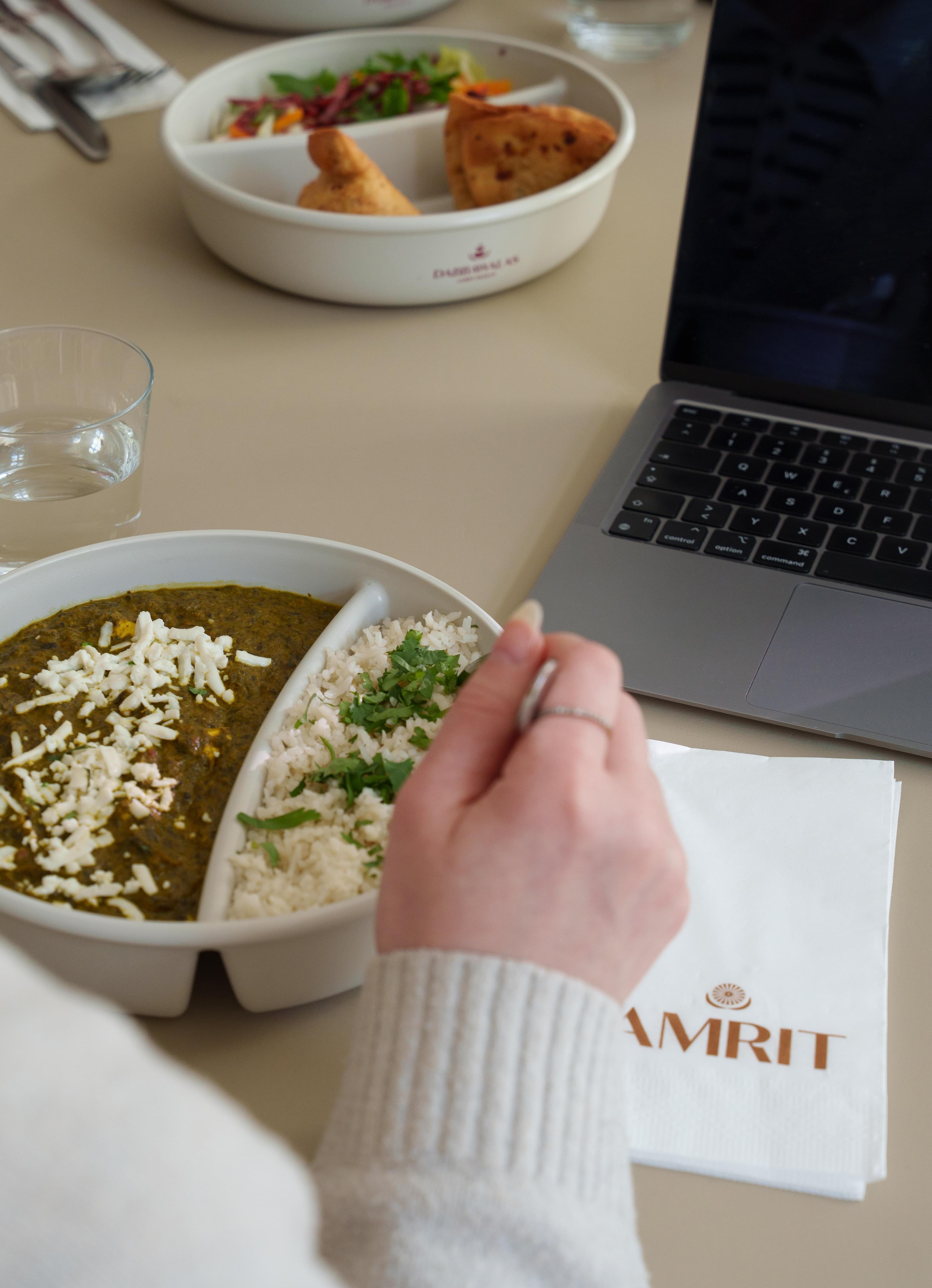 Mitarbeiterin isst indisches Curry am Schreibtisch aus der Office Lieferung