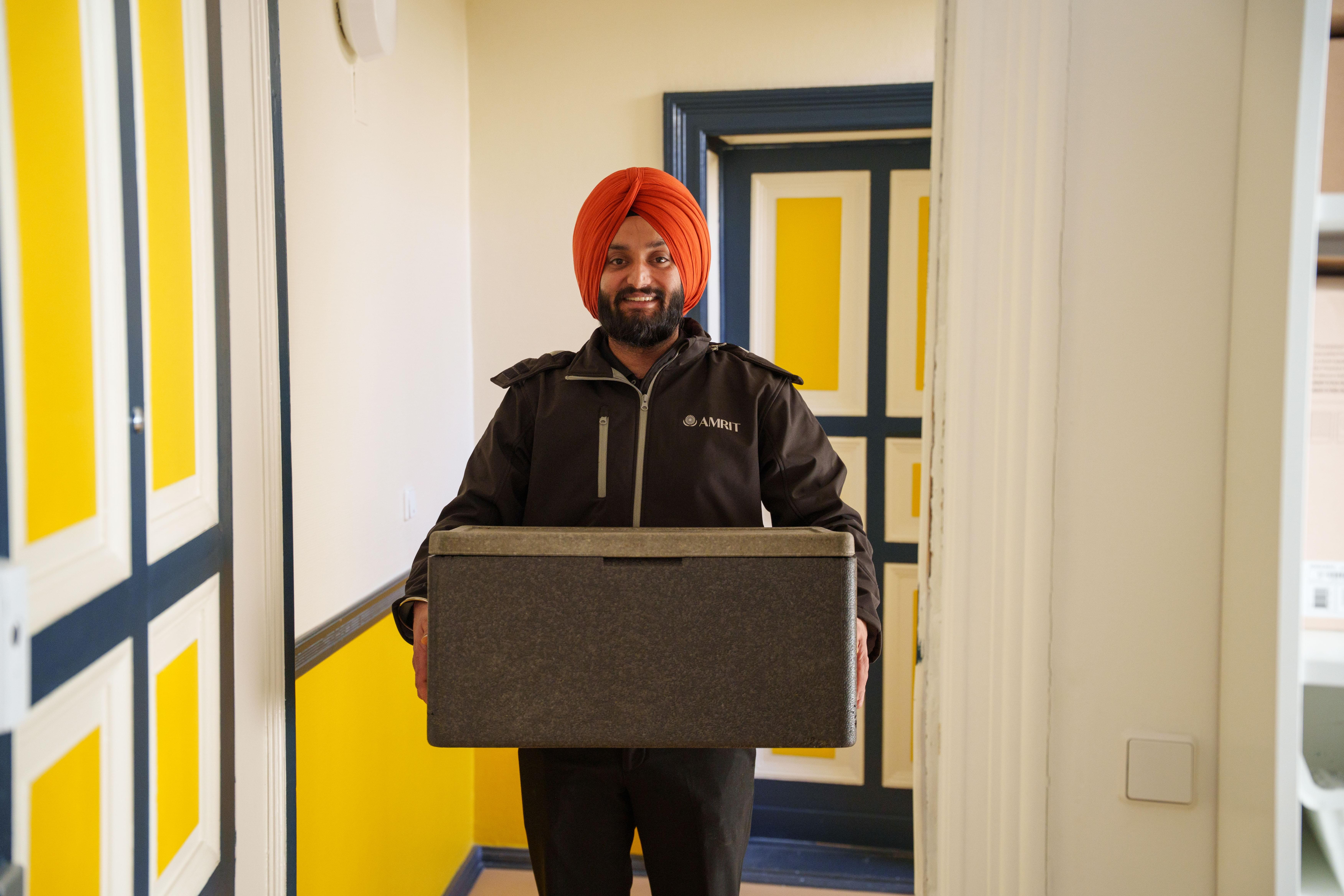 AMRIT Mitarbeiter liefert warme Speisen in der Transportbox zum Crew Catering
